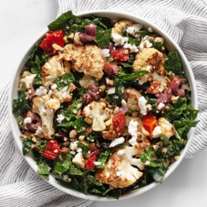 Kale salad with roasted cauliflower tomatoes and olives in a bowl.