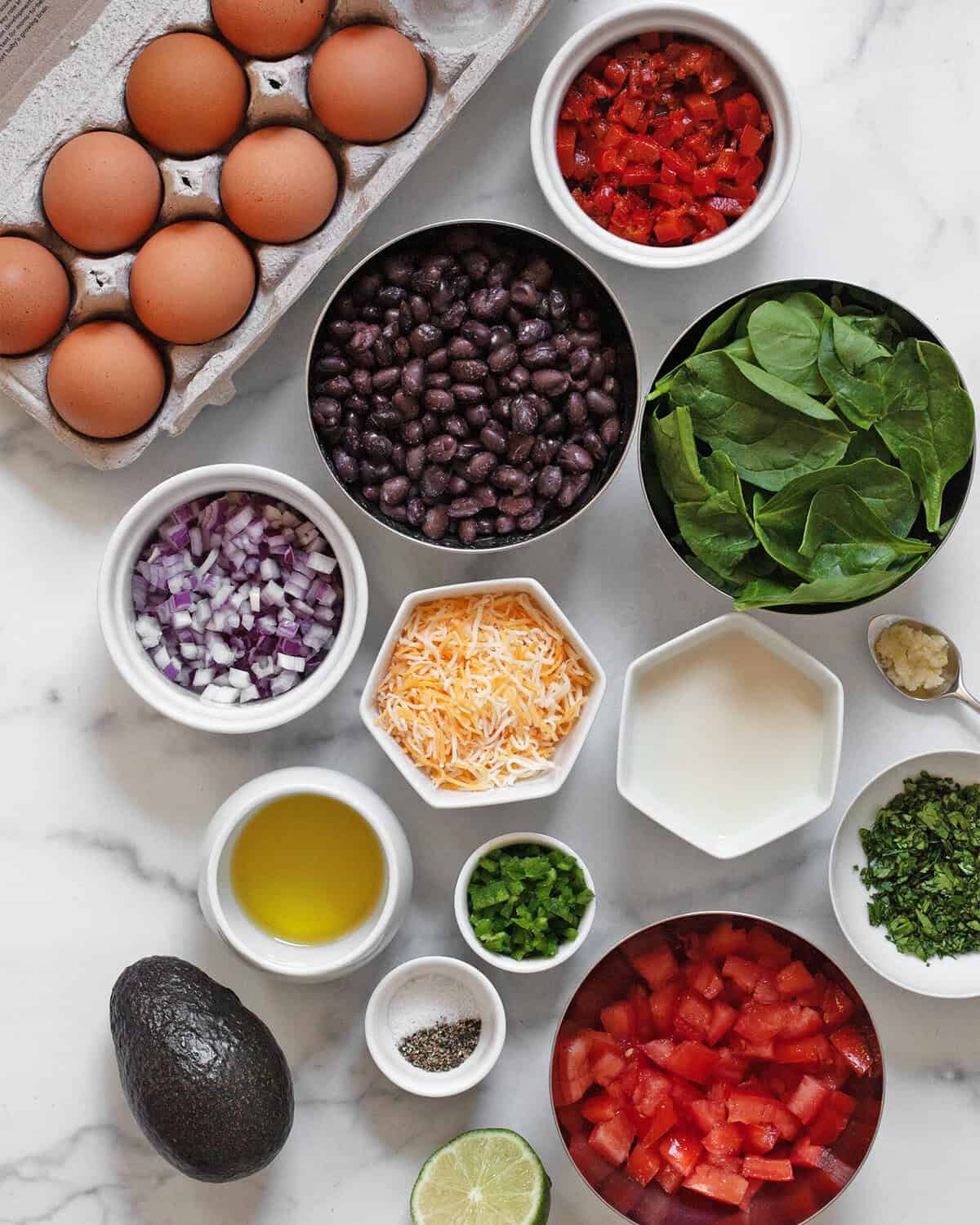 Ingredients including eggs, milk, black beans, roasted red peppers, spinach, shredded cheese, red onions, jalapenos, cilantro, garlic, avocado, salt and pepper.