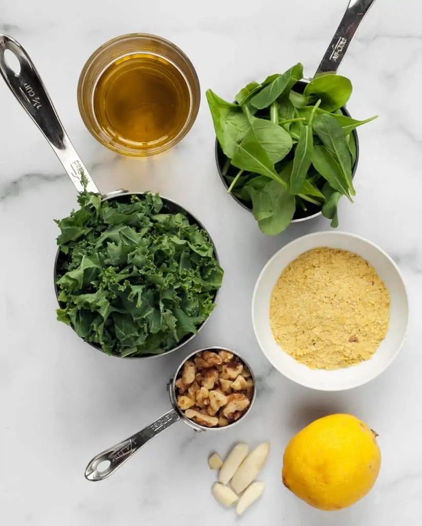 Ingredients for vegan pesto with kale, arugula, nutritional yeast, lemon, walnuts and garlic