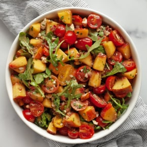 Peach salad with tomatoes, arugula, herbs, almonds and feta in a bowl.