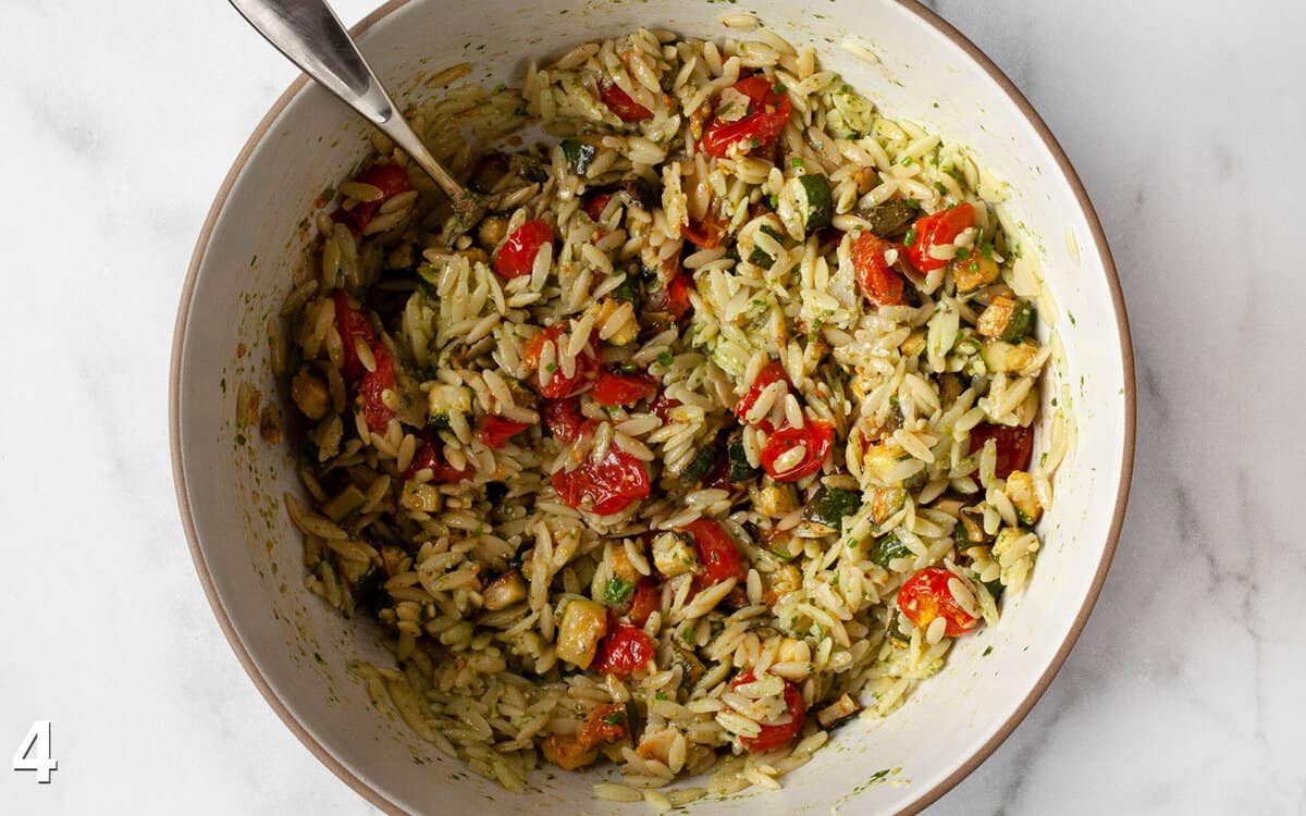 Vegetables stirred into orzo in a bowl.