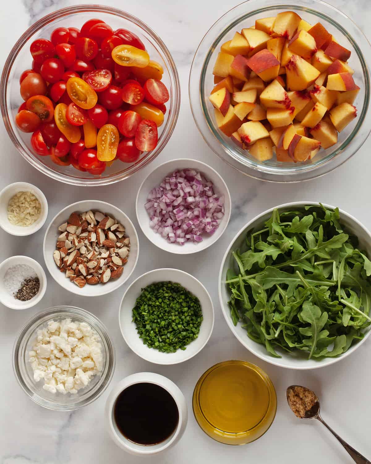 Ingredients including tomatoes, peaches, arugula, feta, almonds, fresh herbs, balsamic vinegar and olive oil.