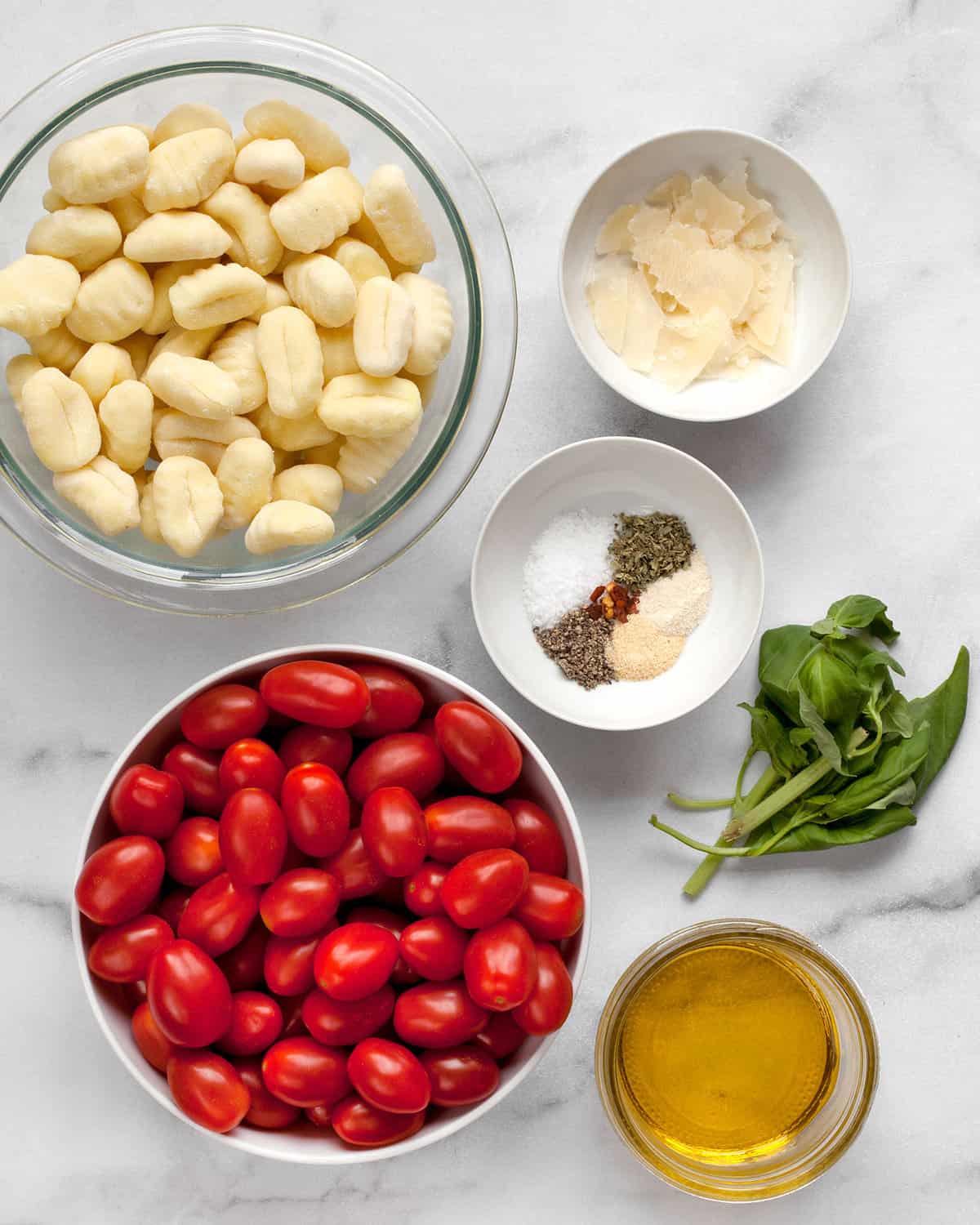 Ingredients including packaged gnocchi, tomatoes, spices, parmesan, basil and olive oil.