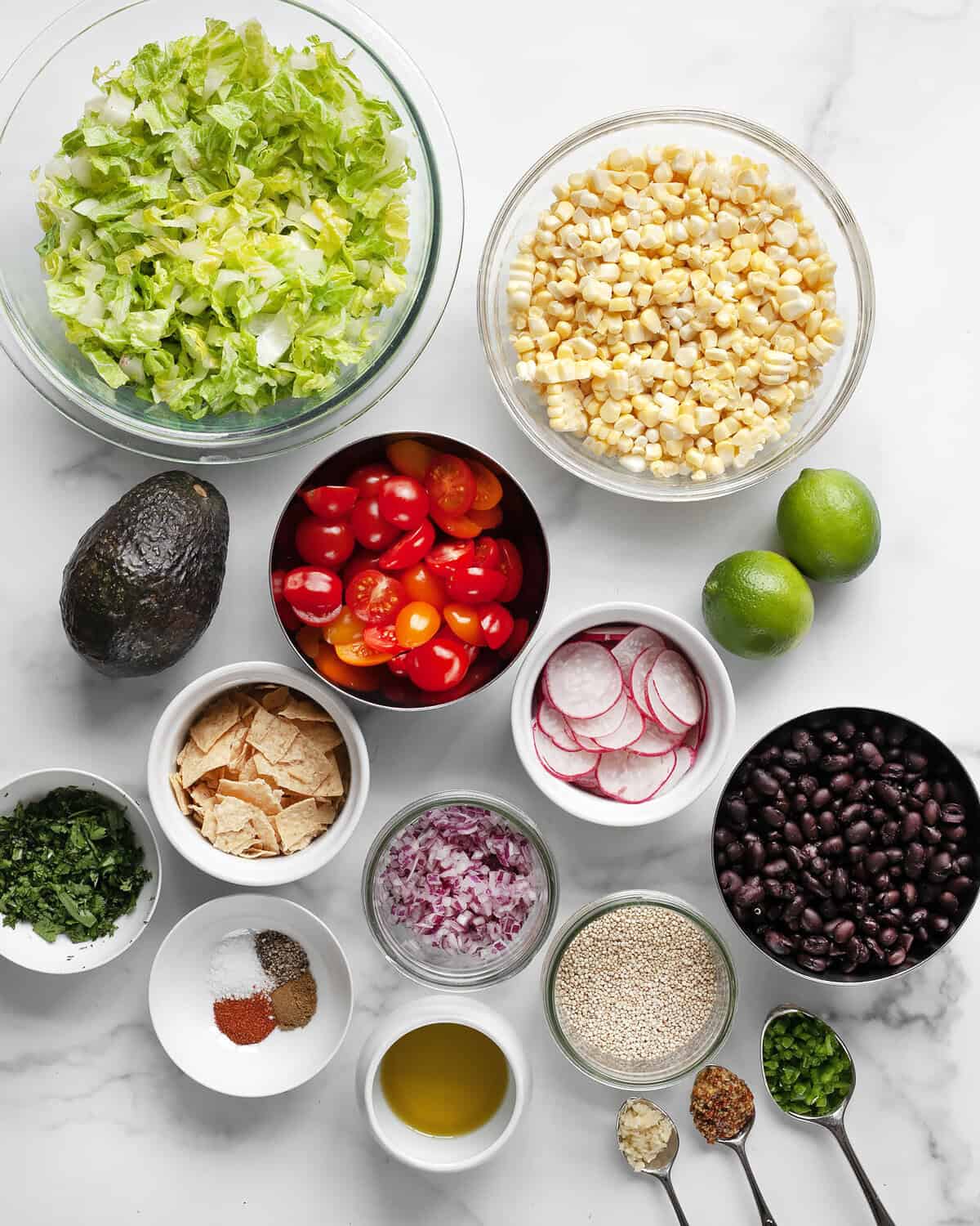 Ingredients including corn, tomatoes, black beans, avocado, radishes, red onions, romaine, limes, spices, garlic, jalapeños, oil and cilantro.