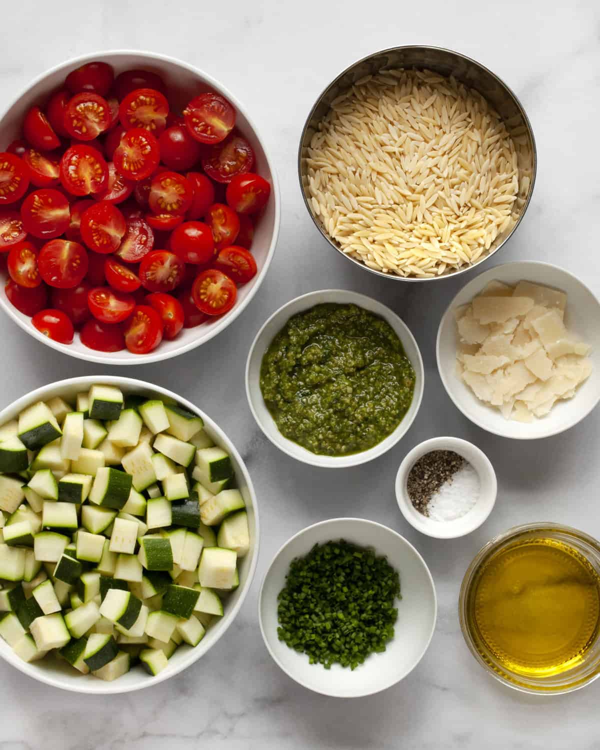 Ingredients including zucchini, tomatoes, orzo, pesto, parmesan, chives, olive oil, salt and pepper.
