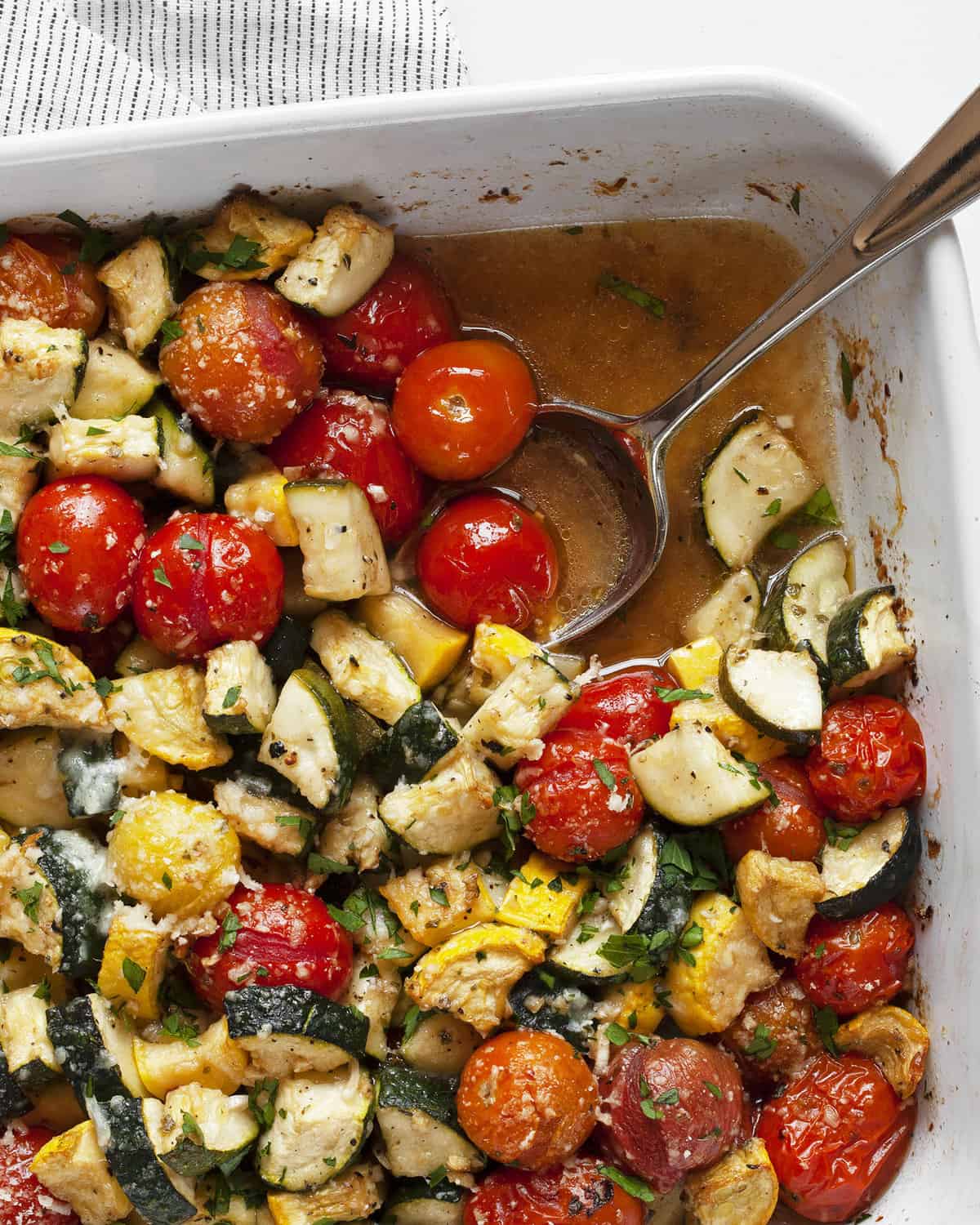 Zucchini tomato bake with spoon in casserole dish.