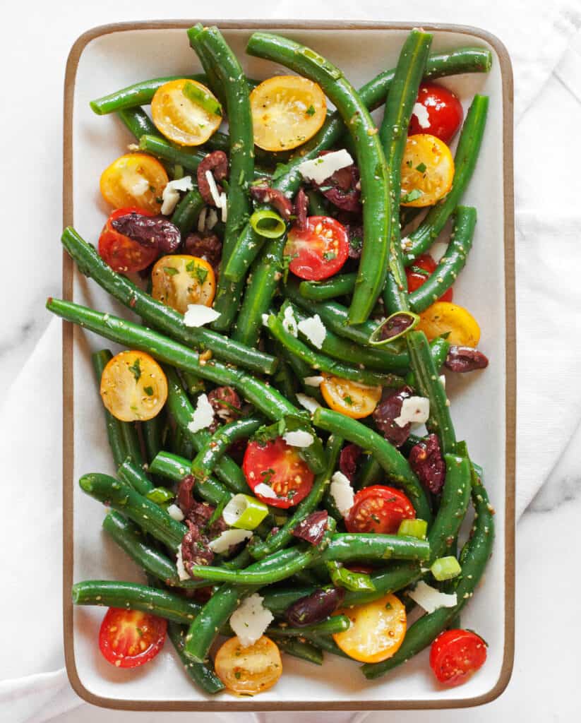 Green bean salad with cherry tomatoes and olives on a plate.