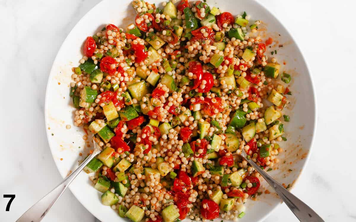 Roasted tomatoes, cucumbers and couscous tossed in a bowl.