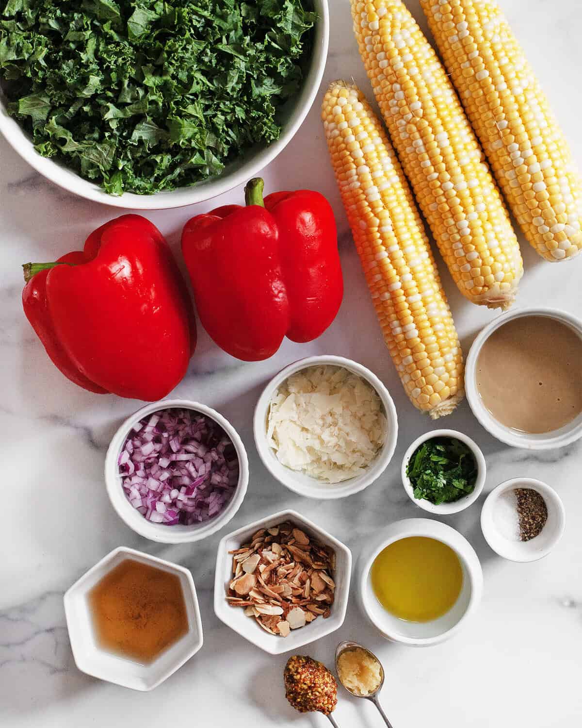 Ingredients including corn, peppers, kale, parmesan, red onions, parsley, almonds, tahini, olive oil, white wine vinegar, salt and pepper.