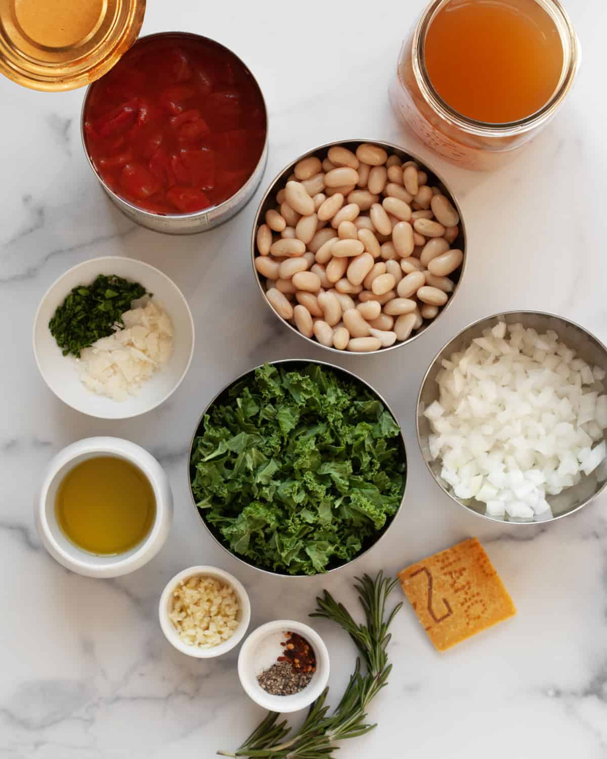 Ingredients including tomatoes, rosemary sprigs, white beans, kale, veggie broth, garlic, parmesan rind, salt and pepper.