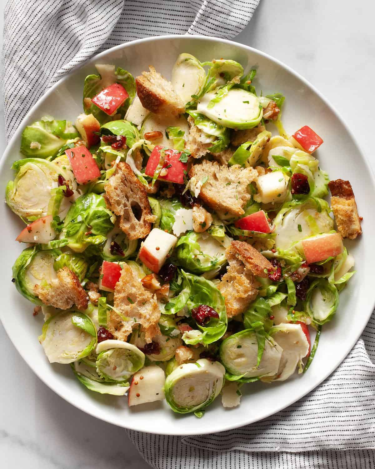 Brussels sprout salad with apples, walnuts, dried cranberries and croutons on a plate.