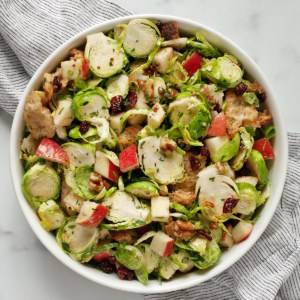 Brussels sprout salad with apples, walnuts, dried cranberries and croutons in a bowl.