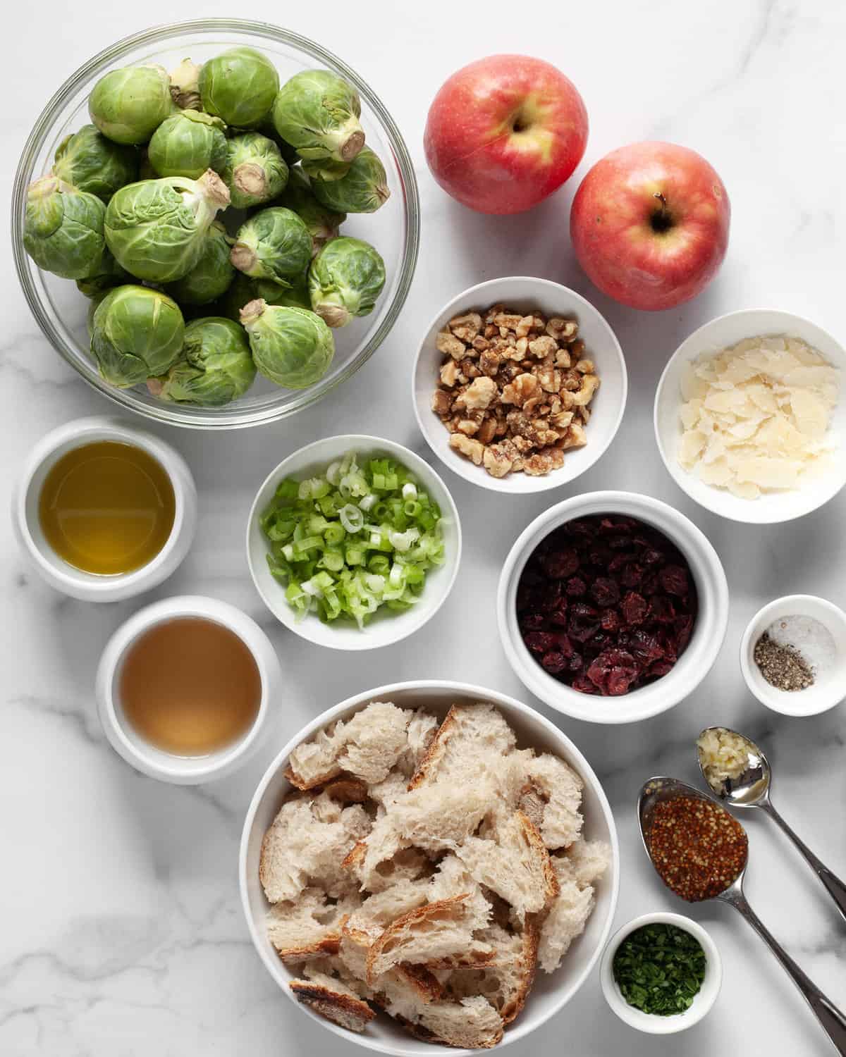 Ingredients including brussels sprouts, apples, walnuts, scallions, bread, cranberries, parmesan, olive oil, white wine vinegar, mustard and garlic.