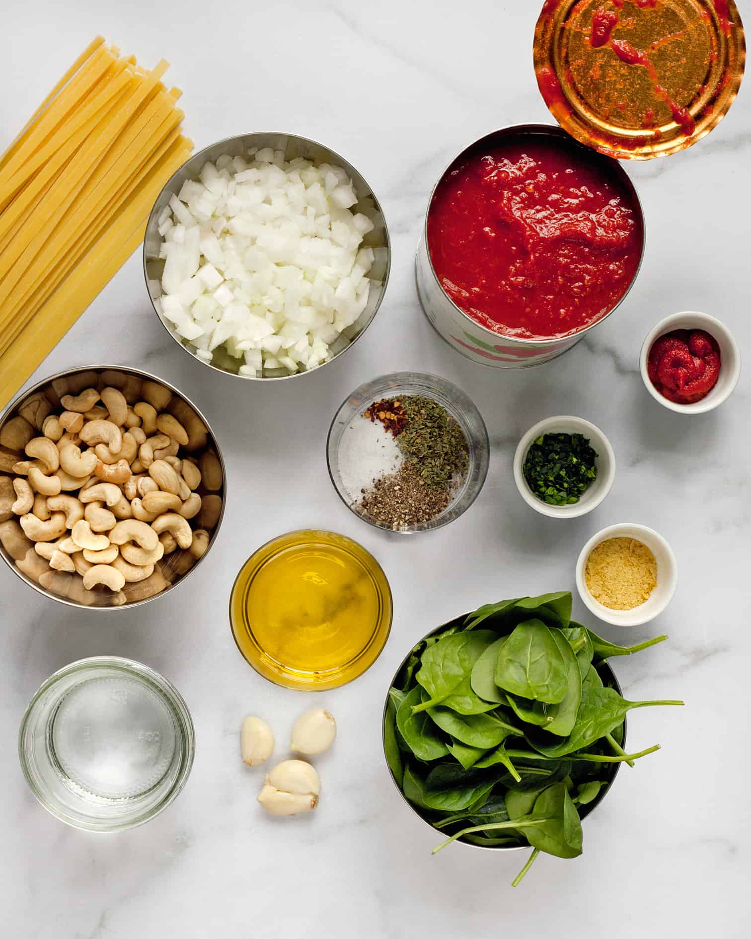 Ingredients for vegan pasta including tomatoes, spinach, garlic, olive oil and cashews