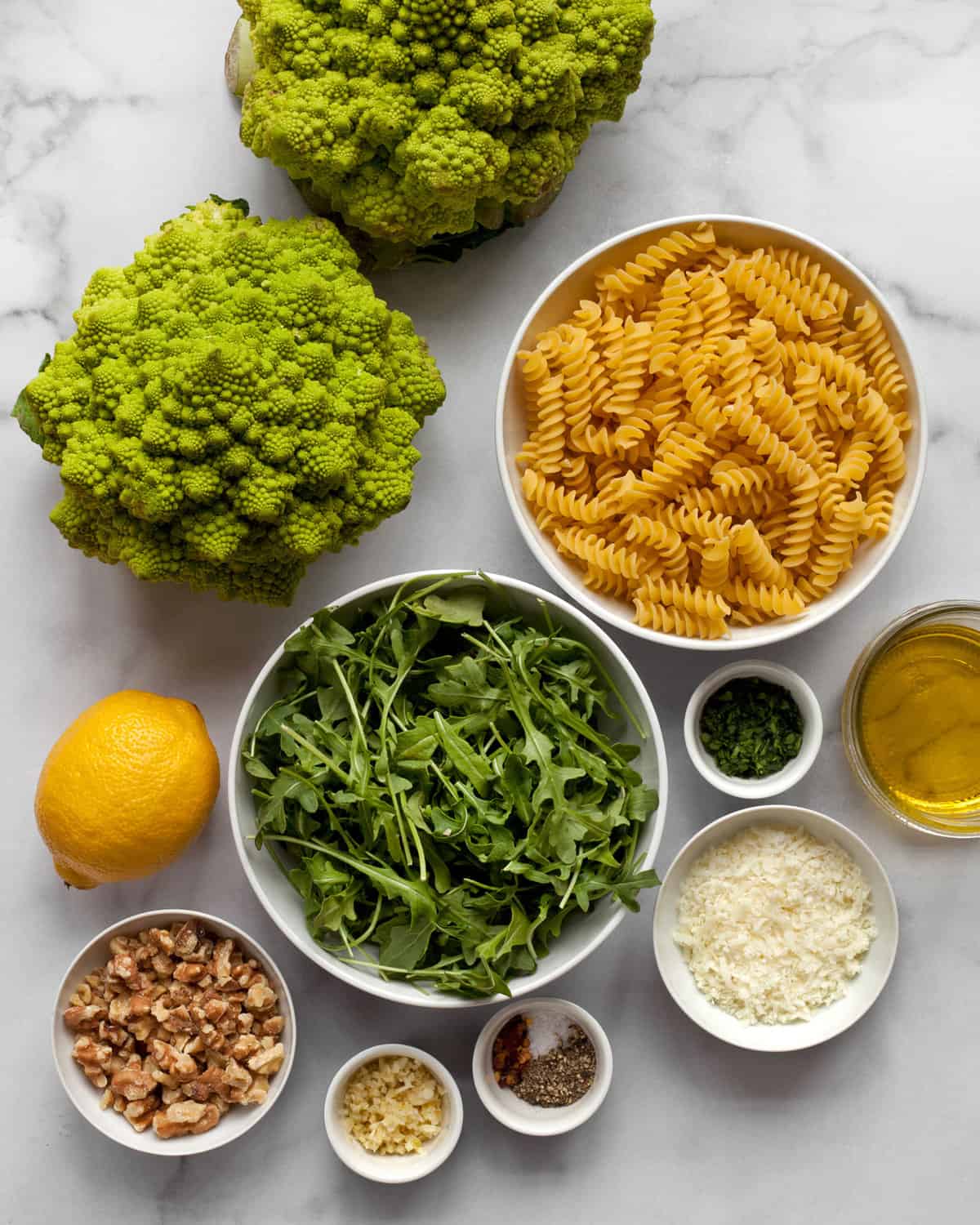 Ingredients including romanesco, pasta, arugula, cheese, walnuts, olive oil and garlic.