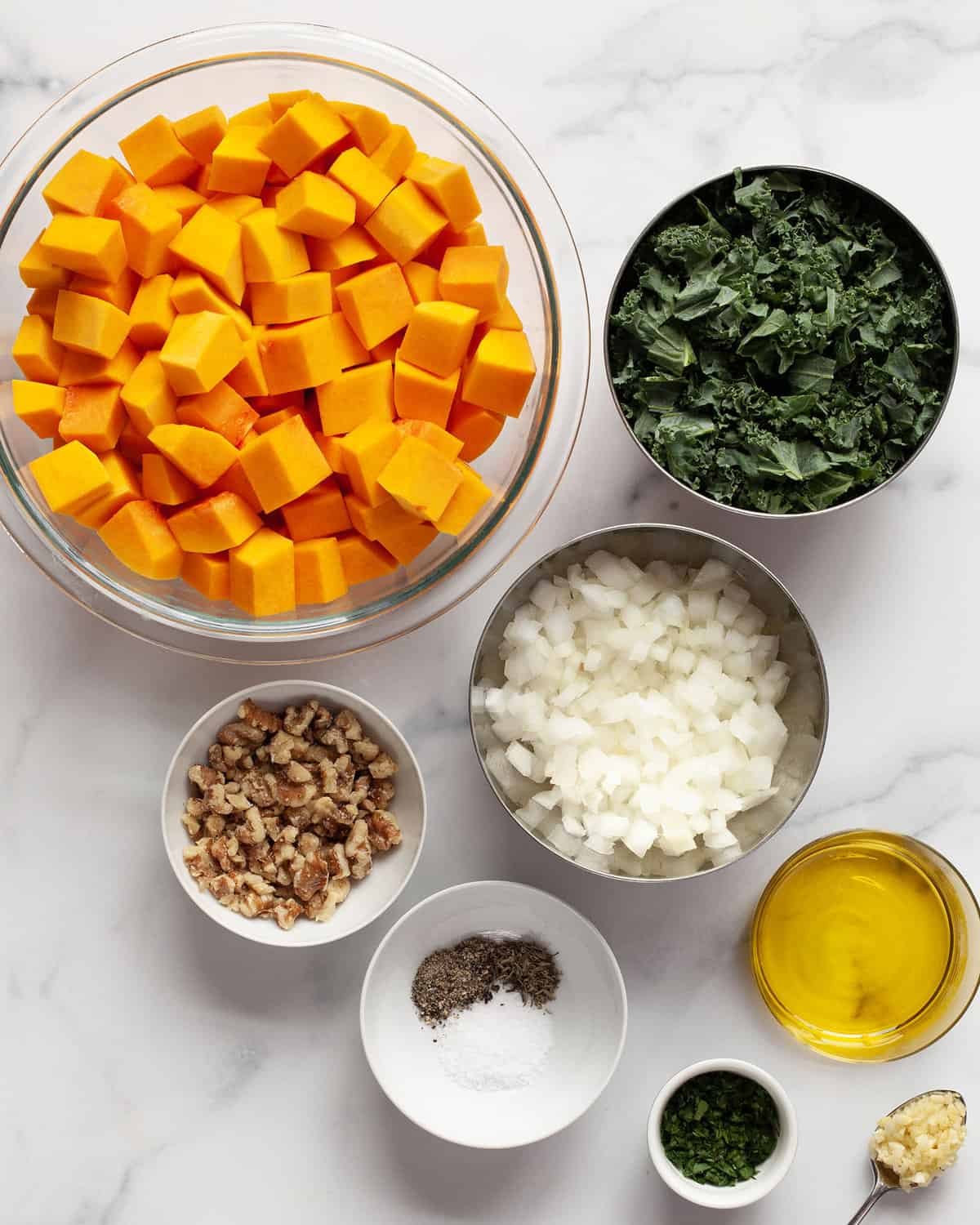 Ingredients including butternut squash, kale, onions, walnuts, olive oil, spices and parsley.