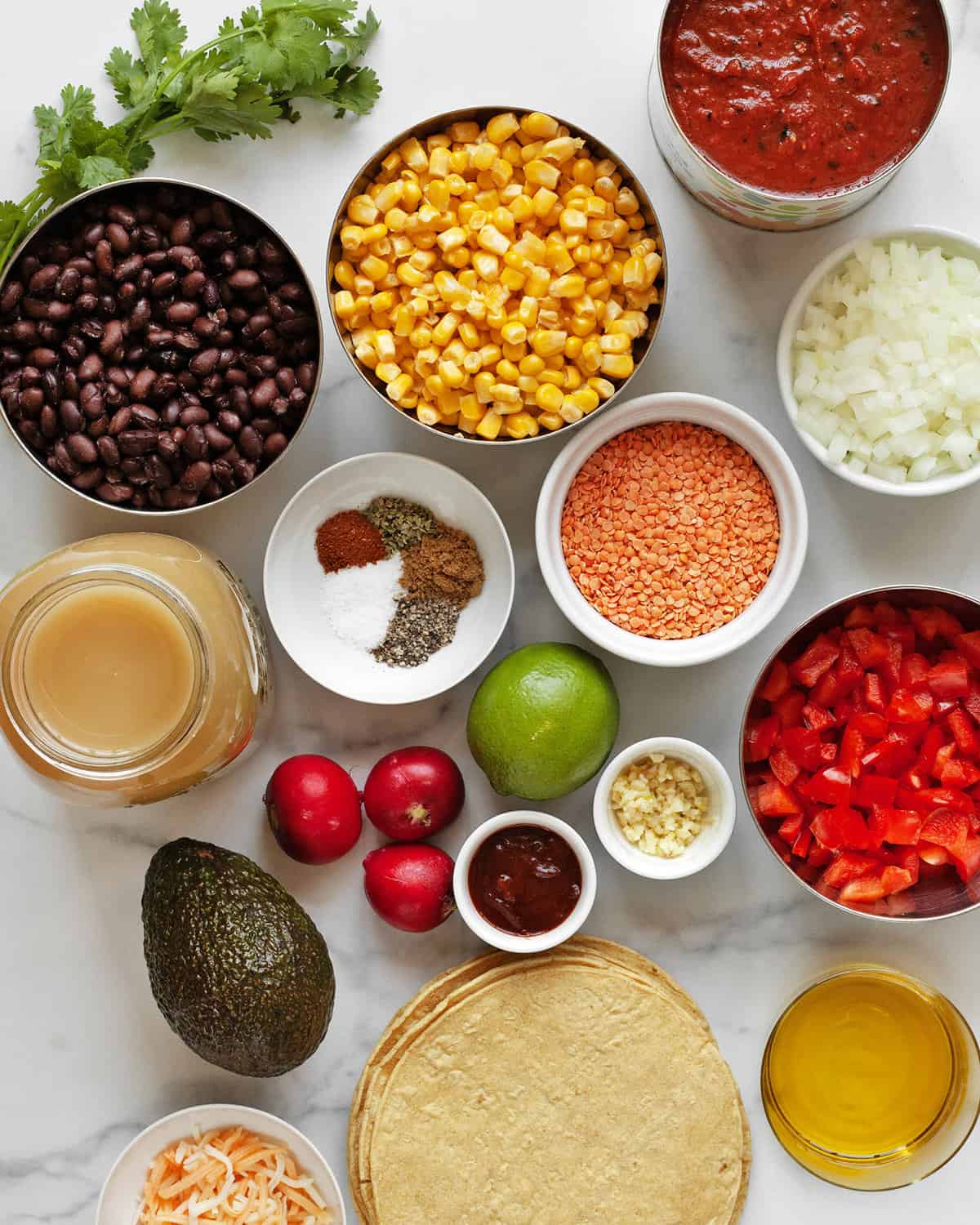 Ingredients including black beans, corn, tomatoes, red lentils, vegetable broth, onions, spices, garlic, adobo sauce and corn tortillas.