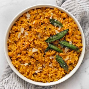 Baked pumpkin risotto in a serving bowl garnished with sage and Parmesan.