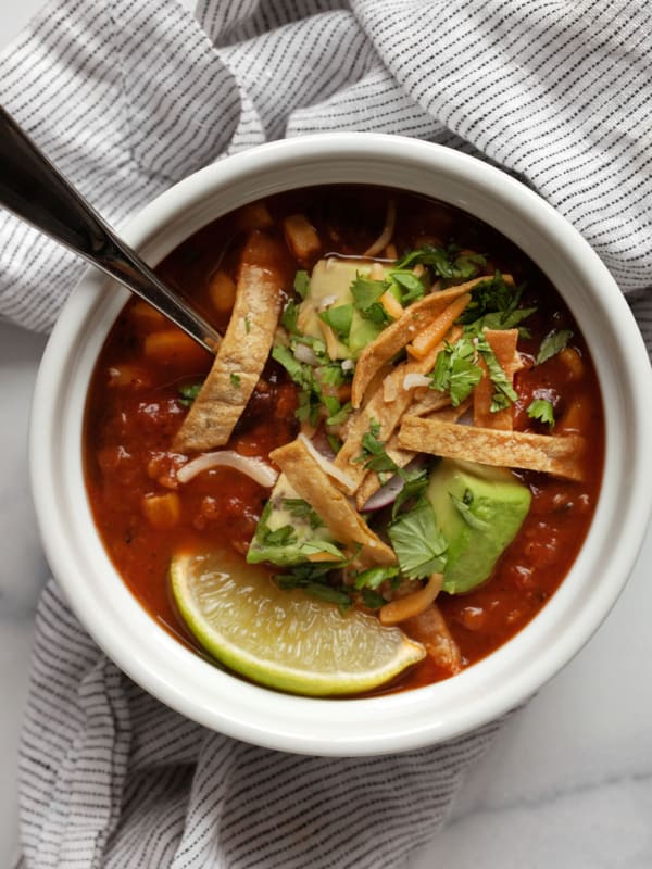 Bowl of tortilla soup topped with avocados, crispy tortilla strips, cheese, radishes and cilantro.