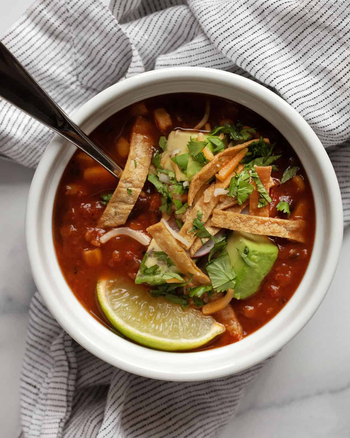 Bowl of tortilla soup topped with avocados, crispy tortilla strips, cheese, radishes and cilantro.