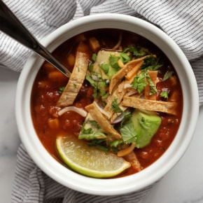 Bowl of slow cooker tortilla soup topped with avocados, crispy tortilla strips, shredded cheese, radishes and cilantro.