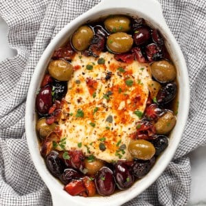 Feta in a baking dish with tomatoes and olives.