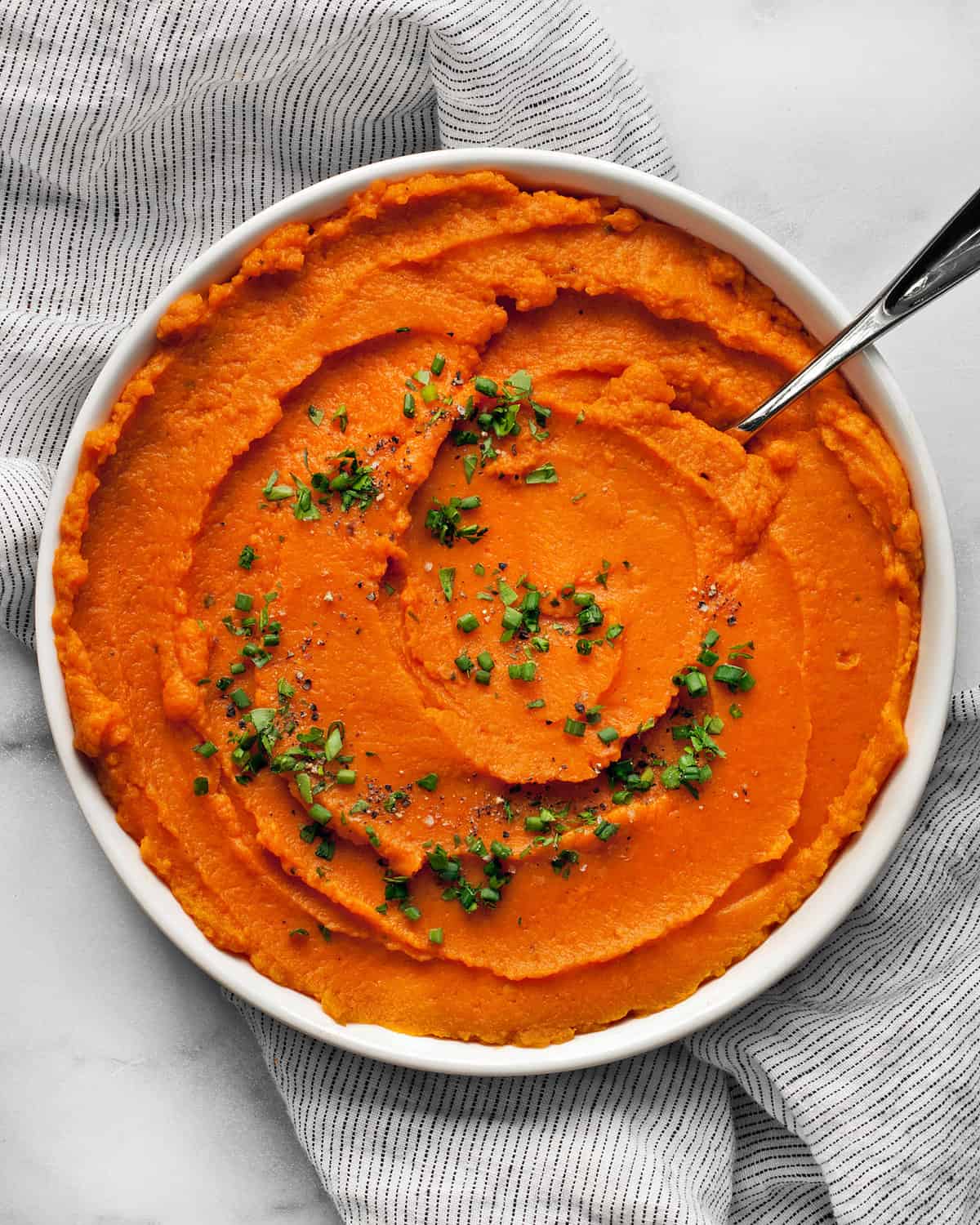 Mashed sweet potatoes in a bowl with fresh herbs.