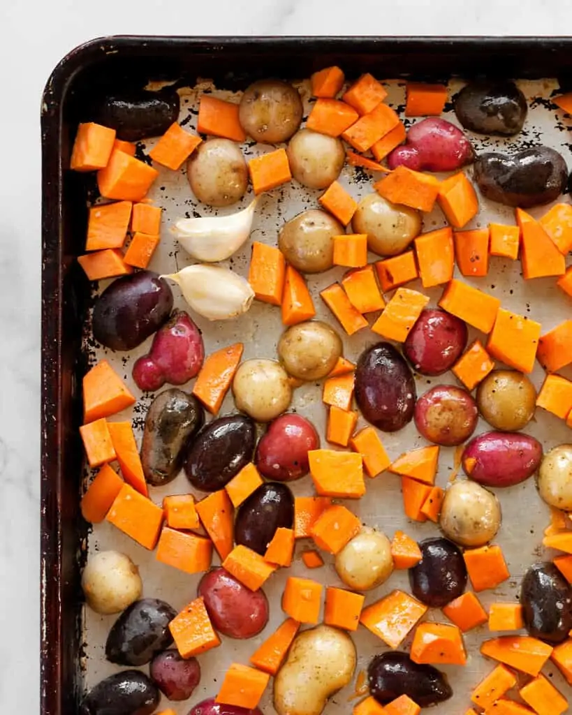 Halved fingerling potatoes and diced sweet potatoes on a sheet pan
