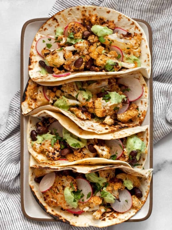 Four roasted cauliflower tacos on a rectangular plate.