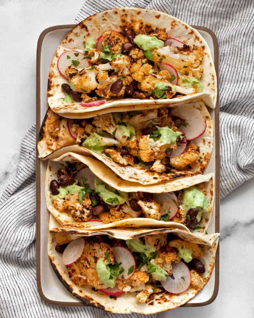Four roasted cauliflower tacos on a rectangular plate.