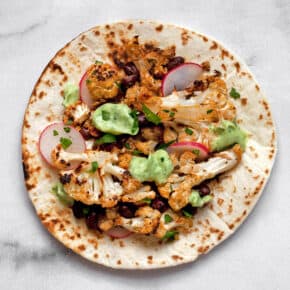 Assembled taco with cauliflower, beans and garnishes.