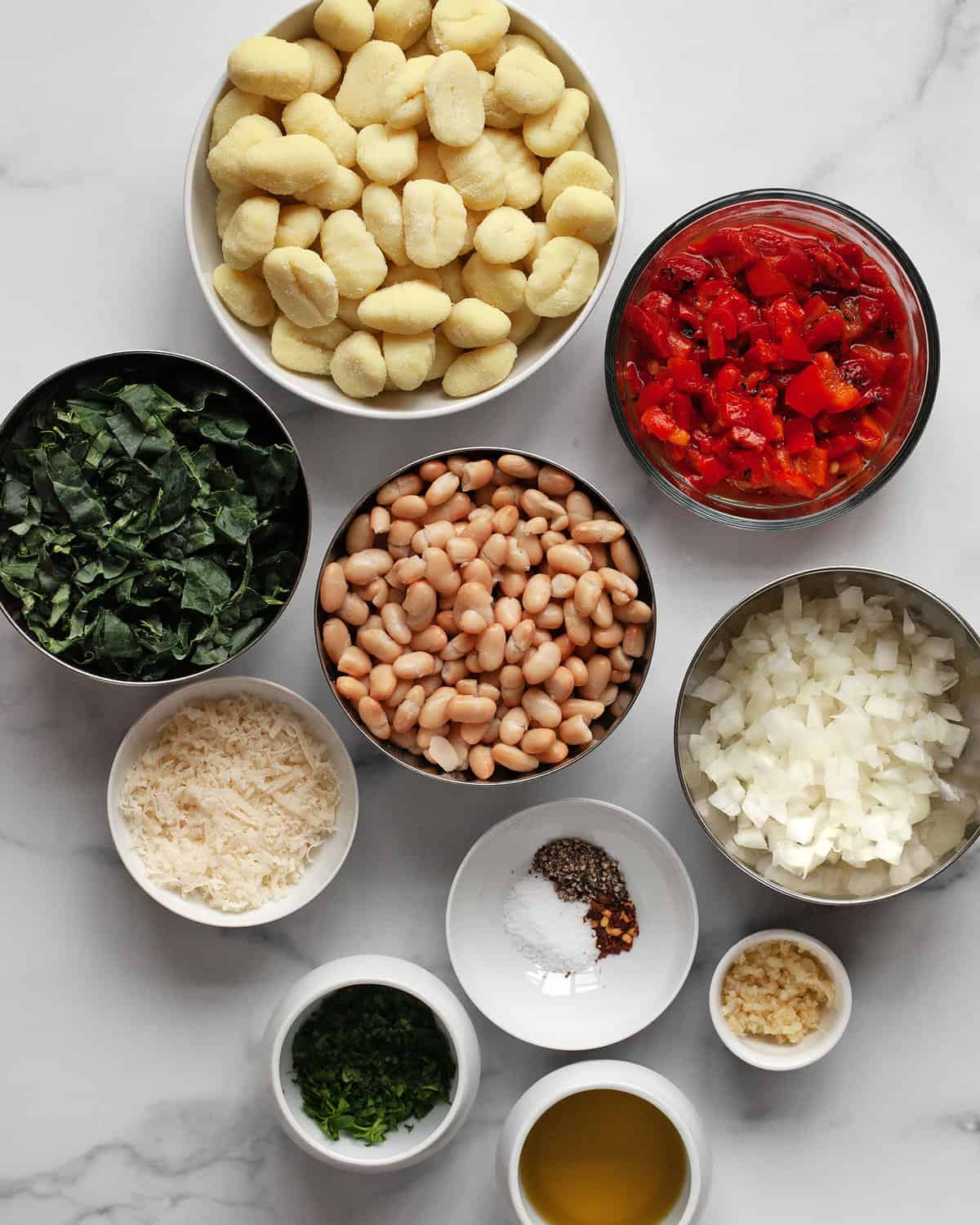 Ingredients including gnocchi, white beans, red peppers, kale, olive oil, onions, parmesan and spices.