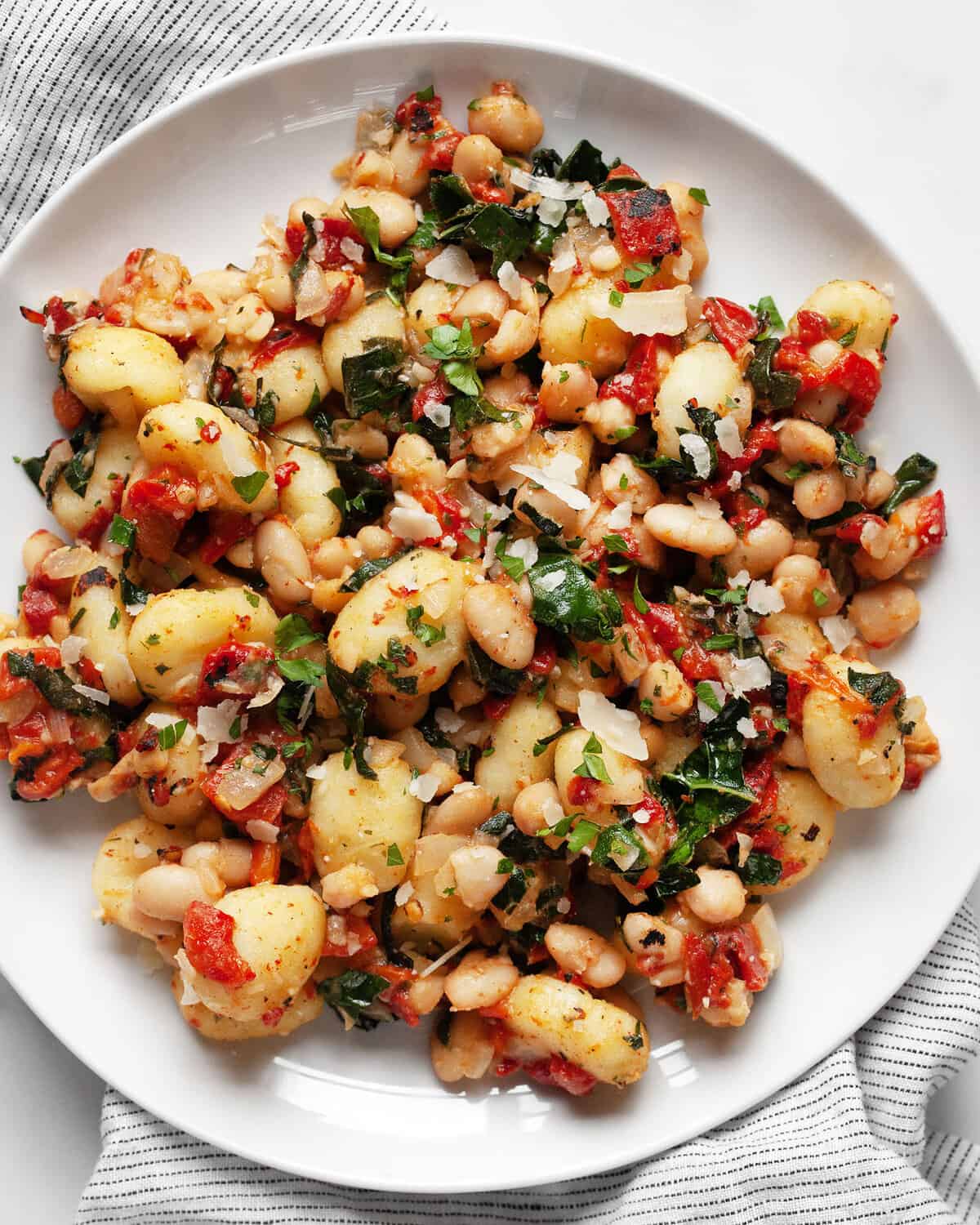 Skillet gnocchi with kale, roasted red peppers and white beans on a plate.