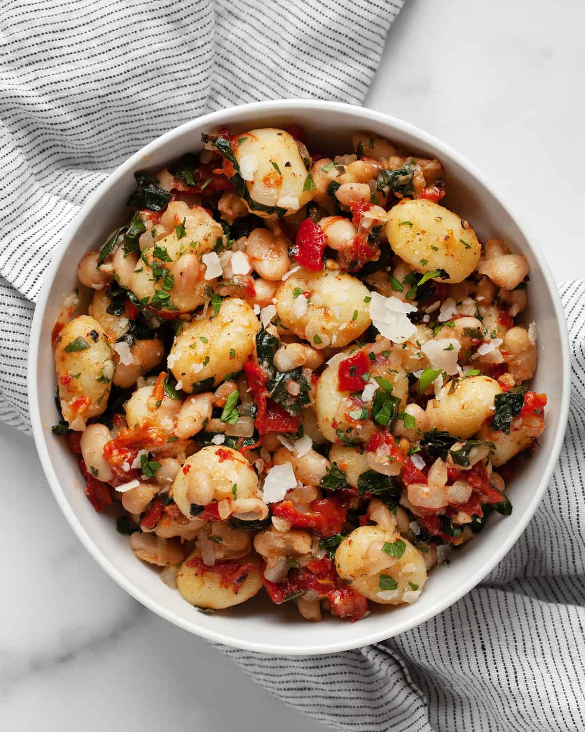 Skillet gnocchi with roasted red peppers, white beans and kale in a bowl.
