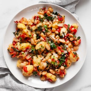 Stovetop gnocchi with roasted red peppers, white beans and kale on a plate.