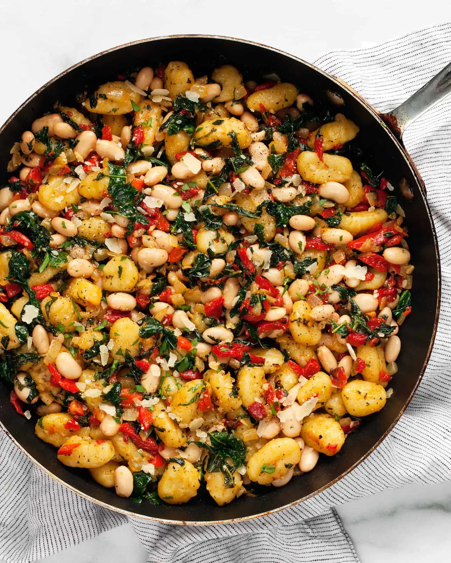 Cooked gnocchi in skillet with white beans, red peppers and kale
