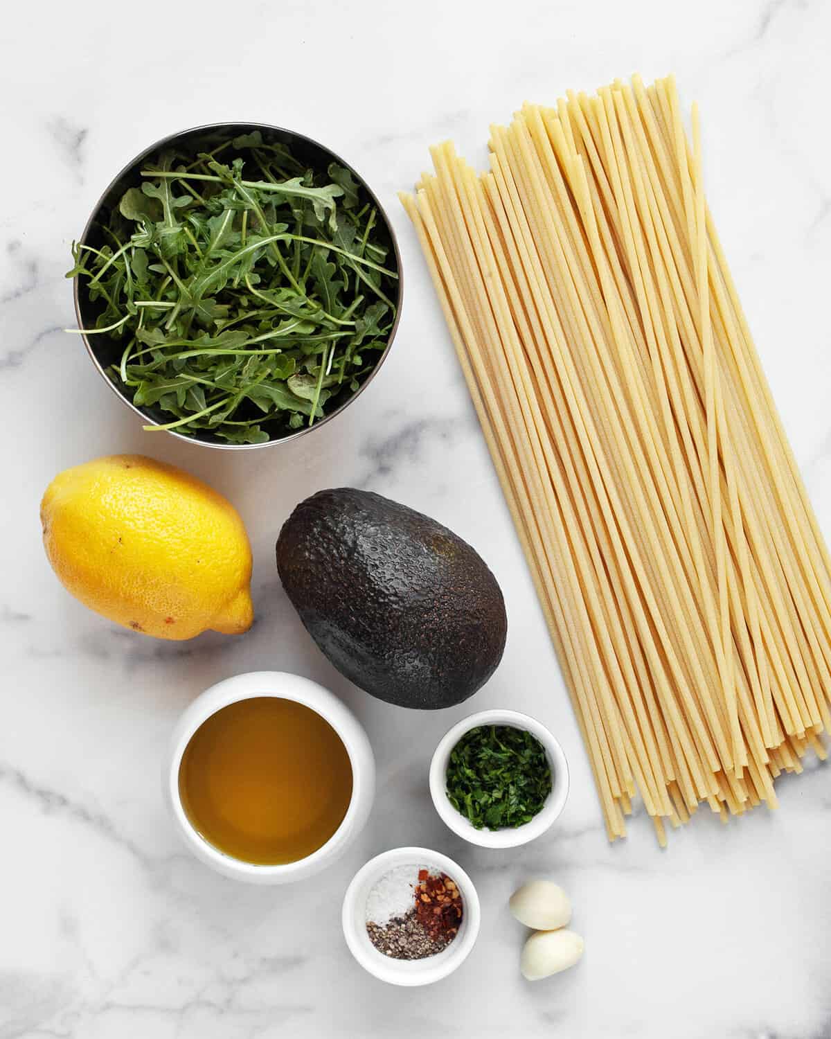 Ingredients including avocado, lemon, garlic, spices, parsley, arugula and pasta.
