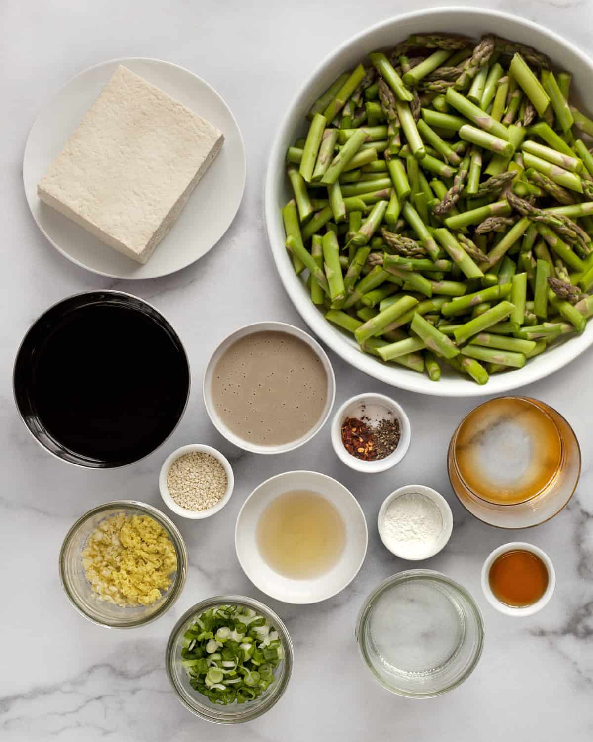 Ingredients including asparagus, tofu, soy sauce, tahini, maple syrup, rice vinegar, scallions, garlic, ginger, oil and seasonings.