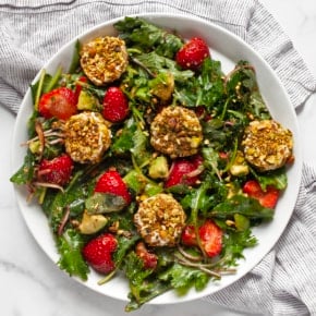 Strawberry salad with pistachio-crusted goat cheese on a plate.