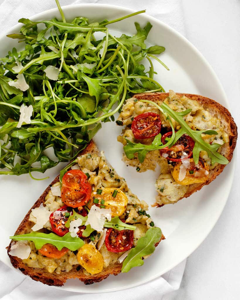 Scrambled eggs with pesto and roasted tomatoes served with arugula salad