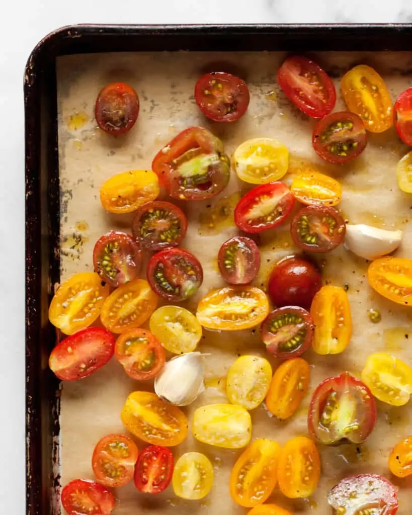 Halved cherry tomatoes and garlic on a sheet pan