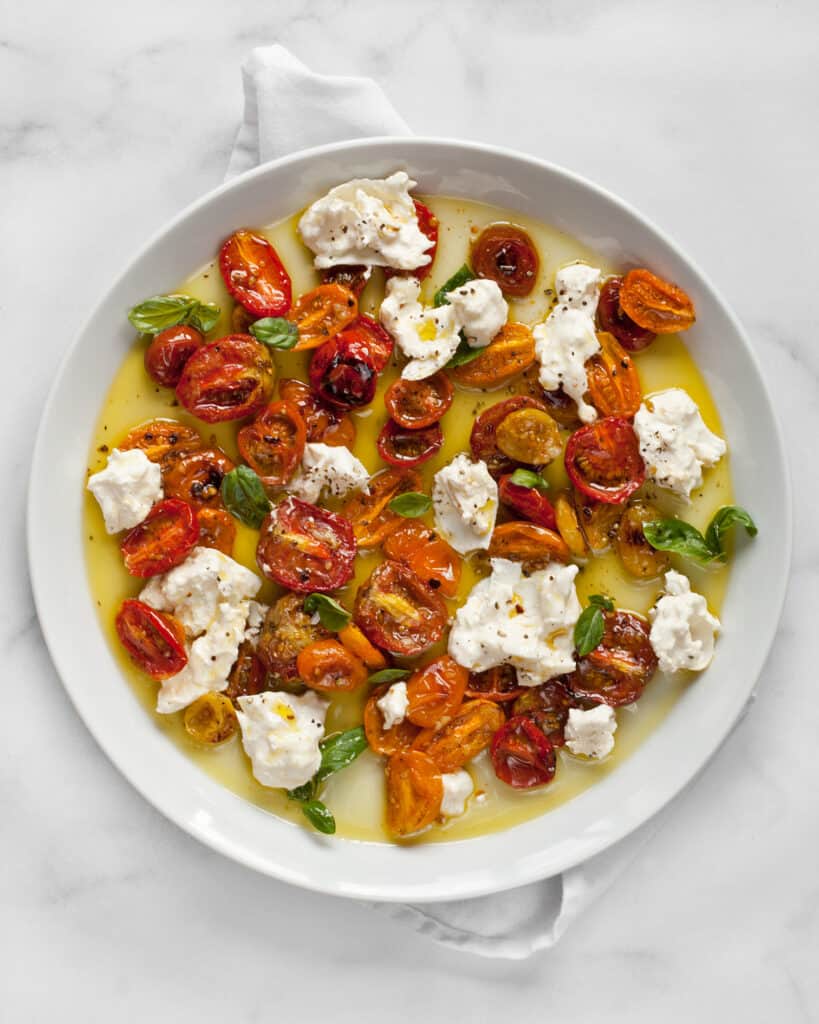 Torn burrata cheese and roasted tomatoes on a plate