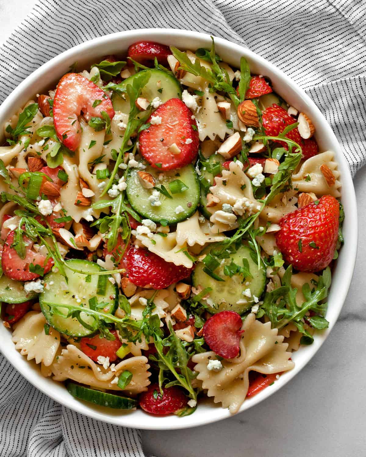 Cucumber pasta salad with strawberries and almonds in a bowl.