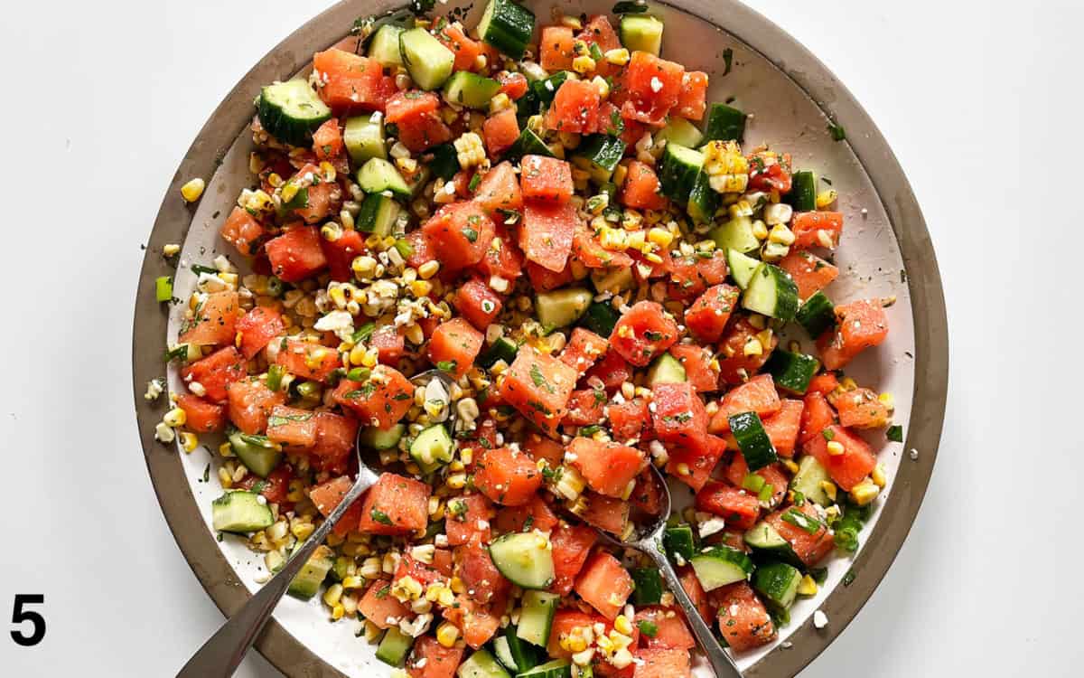 Salad ingredients stirred with dressing in a large bowl.