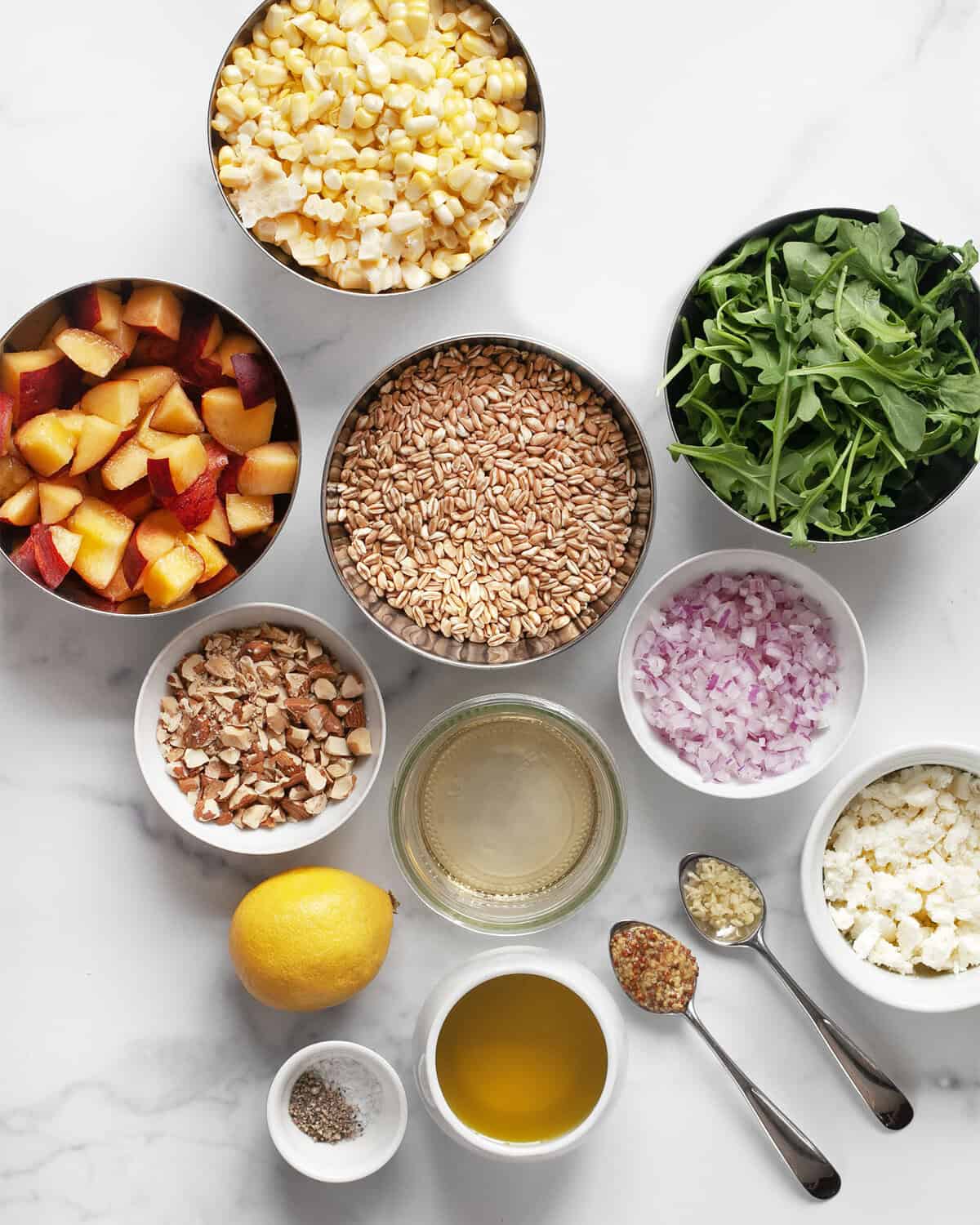 Ingrédients incluant des pêches, des grains de maïs frais, des oignons rouges, du farro, de la roquette, de la feta, du citron, de la moutarde, de l'ail, de l'huile d'olive, du sel et du poivre.