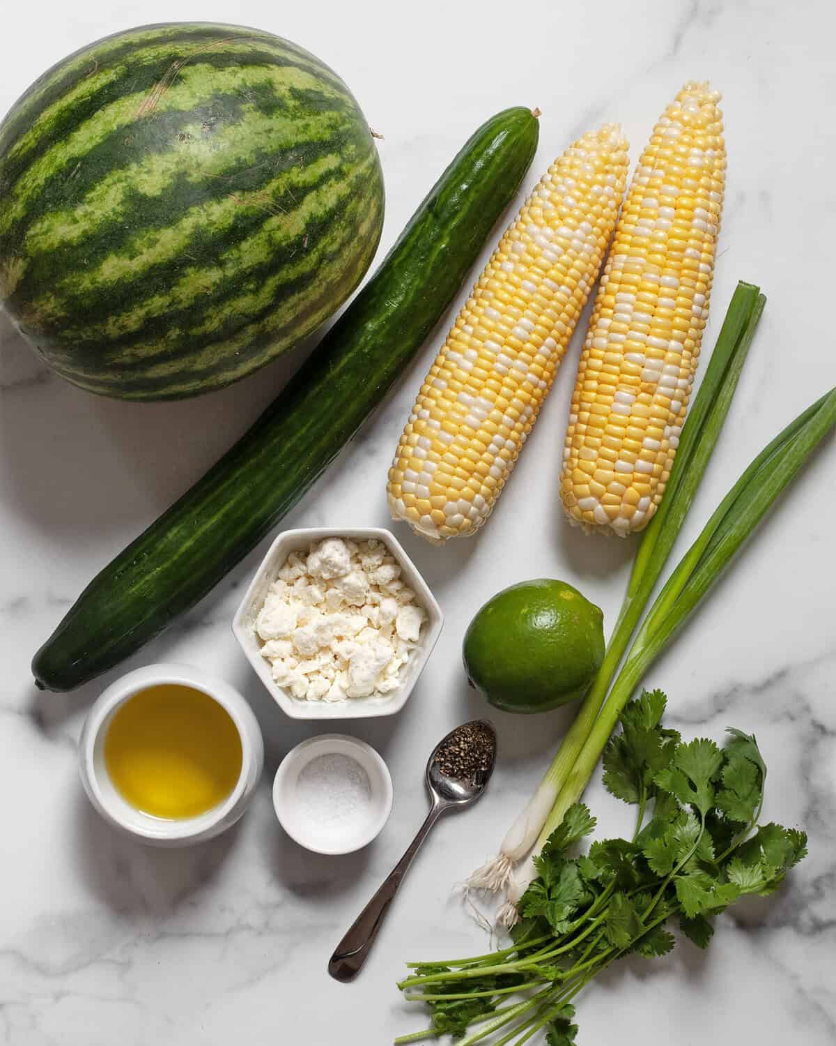 Ingredients including watermelon, cucumber, corn, scallions, cilantro, feta, salt, pepper, lime and olive oil.
