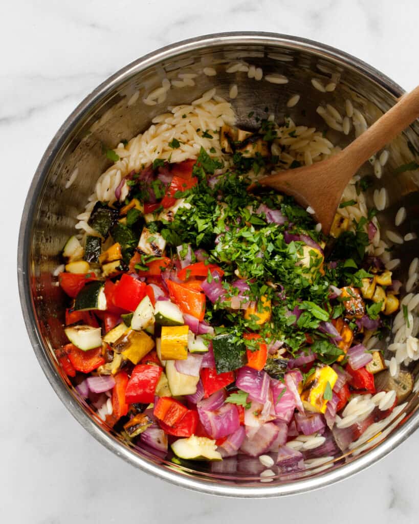 Stirring vegetables and parsley into orzo