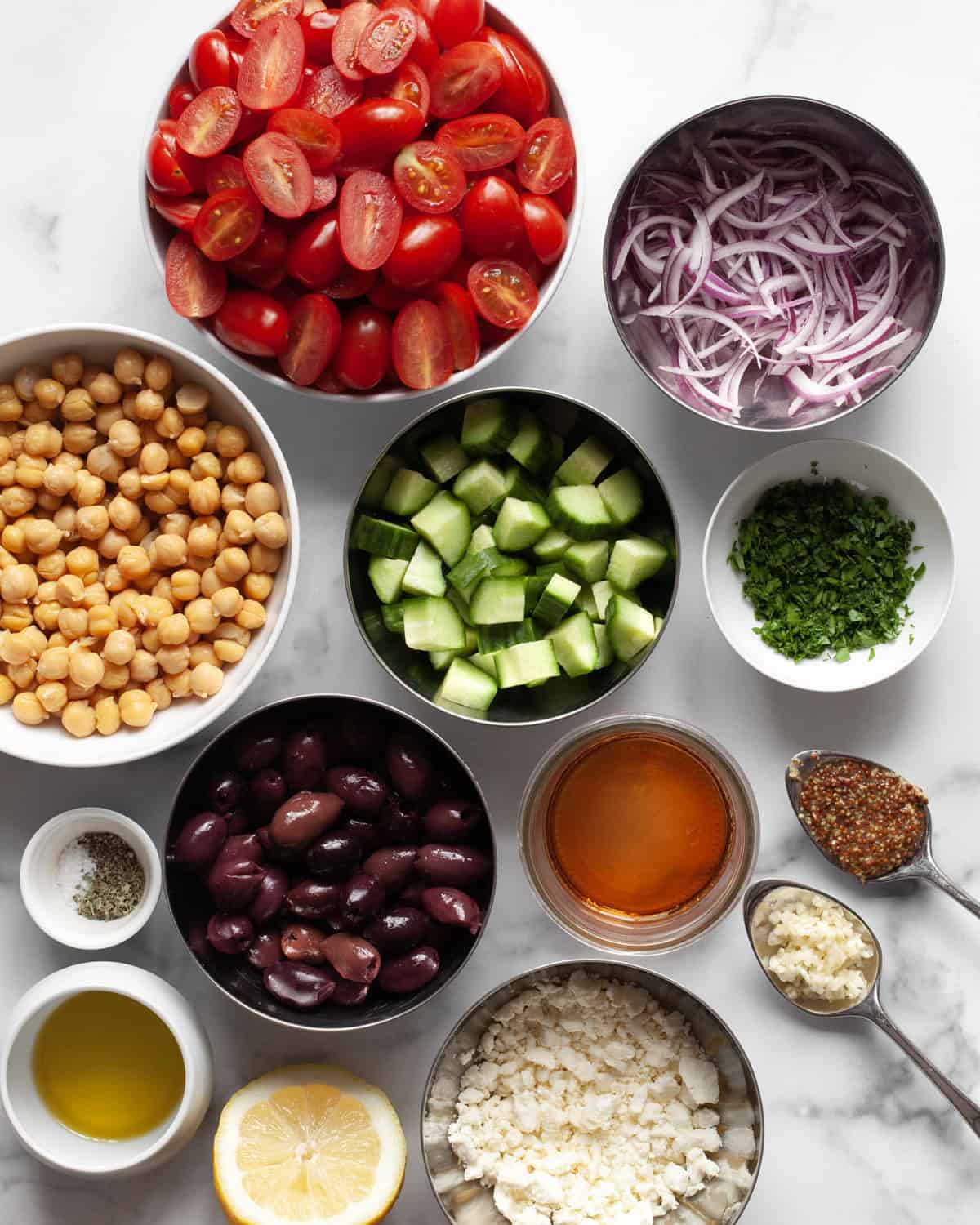 Ingredients including tomatoes, cucumbers, olives, chickpeas, feta, red onions, oil, vinegar, garlic and seasonings.
