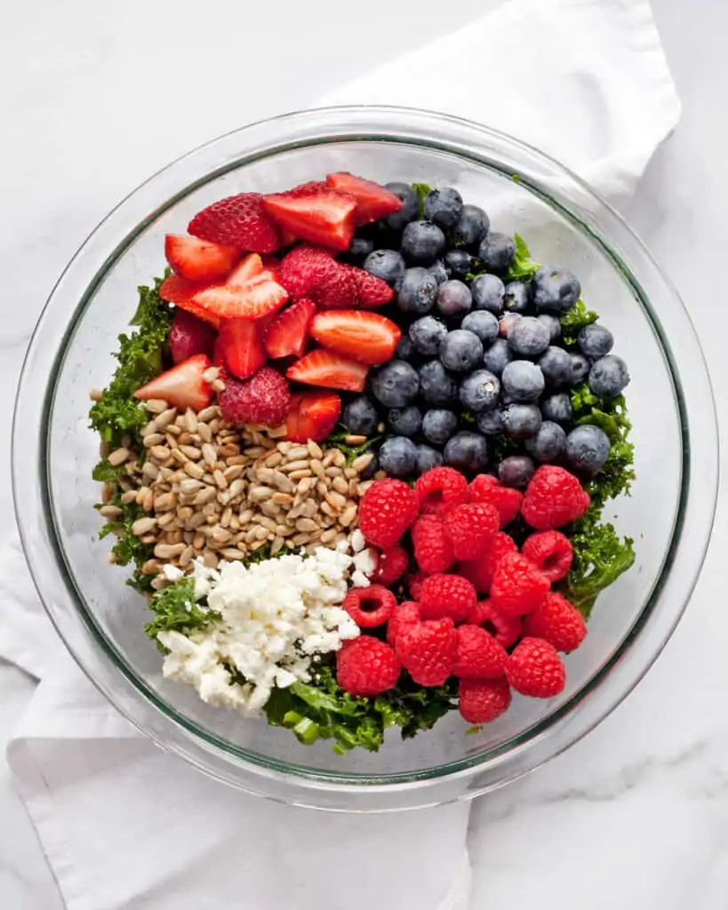 strawberries, blueberries, raspberries, sunflower seeds and feta in a bowl with kale