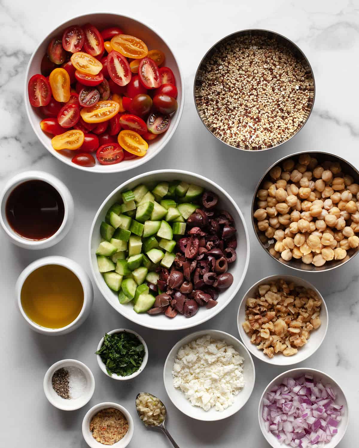 Ingredients including quinoa, chickpeas, tomatoes, cucumbers, olives, red onions, olive oil and red wine vinegar.